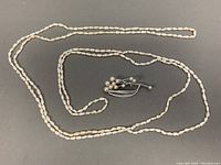 Full view of the long freshwater pearl lariat necklace and pearl brooch placed side by side on a gray surface.