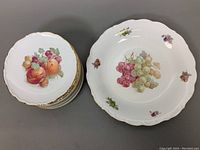 Top view of stacked dessert plates beside single serving plate, all decorated with fruit designs and gilded edges.