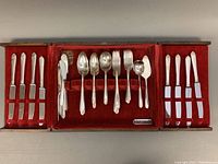 Full view of vintage Community Plate flatware arranged in a wooden chest with red velvet lining, showing knives, forks, spoons, and serving pieces.