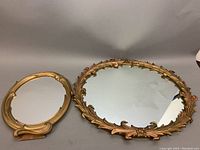 Two vintage ornate Syroco mirrors side by side on grey surface showing overall size and condition.