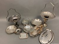 Overview of all silver plated servingware items including footed vases, trays, bowls, and dishes on table surface showing shape and decorative features