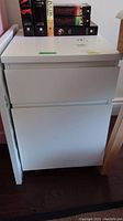 White wood filing cabinet closed showing clean front and top with some books on top.