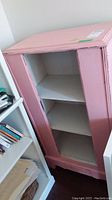 Full view of the antique distressed pink wood cabinet showing the front and sides in the room.