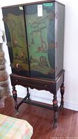 Front view of Chinese wood cabinet with painted doors showing landscape scenes and decorative hardware.