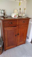 Front view of antique pine cabinet with two top drawers and two doors below, showing wood grain, metal handles, and latch hardware.
