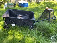 Full side view of the black Woods folding garden cart wagon on grass showing frame, wheels, and pull handle.