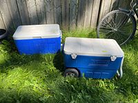Two Coleman coolers side by side on grass, one smaller and one larger with wheels and handle