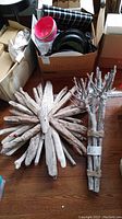Two driftwood decor pieces: a round starburst wall hanging and a tied bundle of driftwood sticks.