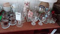 Wide view showing the entire lot: flutes, martini glasses, wine glasses, shot glasses, water glasses, ramicans and two vases with seashells inside.