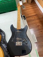 Top-down image of the black electric guitar showing the headstock, neck, and body with noticeable wear and missing strings.