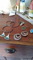Photo showing various bracelets and earrings on a wooden surface including enamel decorated items and bangles.