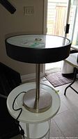 Modern table lamp with cylindrical metal base, wooden trim around glass top, photographed on white round table indoors