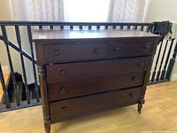 Front view of the mahogany dresser showing four drawers with round knobs and turned front legs, scratches visible on the top surface.