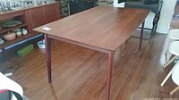 Full view of teak table from front left angle showing overall design and leg style
