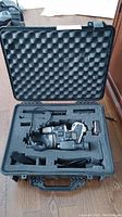 Opened Pelican case containing Canon L1A video camera, battery, and cables inside foam cutouts.