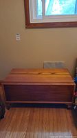 Closed pine blanket box showing wood grain, rectangular shape, and small wheels.