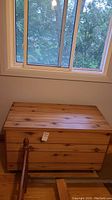 Closed wood panel blanket box under window showing natural wood grain and metal legs
