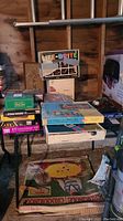 Wide view showing stacked vintage board games with Life-Brite prominently on top, along with other games below and vintage Croquinole game boxes on the floor.