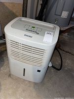Front and side view of a white Danby dehumidifier on concrete floor, showing front grille and top control panel.