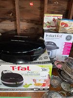 Photo of T-fal ActiFry air fryer box, Hamilton Beach grill on top, Instant Pot in box behind, Starfrit apple peeler box, and lobster dinner set silver pieces on table.
