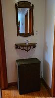 Photo showing full setup against wall: wood framed mirror, demi lune shelf underneath, faux wicker hamper below shelf
