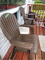 Two brown resin Adirondack-style lawn chairs on a wooden porch floor near a house wall.