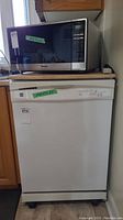 Frontal image of white Kenmore portable dishwasher with wood top, wheels visible, control panel on front.