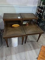 Two matching retro wooden two-tier end tables shown stacked, medium brown wood with defined chevron grain pattern on top surfaces, tapered legs with brass feet.