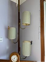 Full view of the floor to ceiling expandable lamp showing three cylindrical cream-colored fabric shades mounted on brass arms, attached to a dark wooden pole.