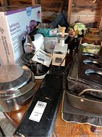 Lot overview showing unopened Rival roaster oven box, Sunbeam Mixmaster mixer with bowls, metal roasting pans, muffin tins, table lamp, Rival grinder, and pottery jug in wooden box.