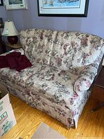 Wide shot of floral two-seater sofa bed with tufted back and skirt, showing handmade throw on seat.