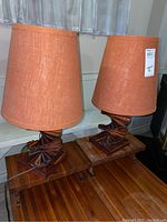 Pair of table lamps showing overall look, each with orange fabric shades and dark stained wood bases on a wooden table.
