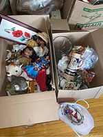 Photo of two cardboard boxes containing dolls in traditional clothing, a rocking tin bear, wooden chest, framed needlepoint, animal figurines, a bird wall plaque, cut glass vase, coasters, and a beer stein.