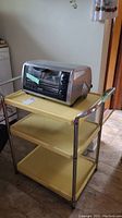 Photo showing the Black & Decker toaster oven on top of the vintage yellow metal kitchen cart with three shelves and chrome handles.