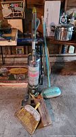 Photo showing upright Hoover Windtunnel vacuum with PowerAir Turbo brush next to vintage General Electric floor polisher and metal dustpan on concrete floor.