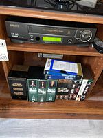 Hitachi VHS player Model FX6505 with remote and VHS tape sets on shelves