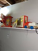 Shelf displaying vintage toys including Fisher-Price teaching clock, red tin radio, wooden horse, white pull toy vehicle with blue wheels.
