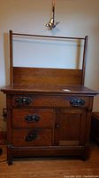 Front view of vintage solid wood wash stand showing four drawers and a cupboard with metal knocker-style knobs.
