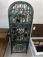 Front view of the black metal wine rack with several bottles placed inside, showcasing the ornate scrollwork design and bottle slots.