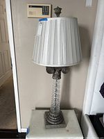 Front view of Art Deco-style table lamp showing glass base with metal embellishments and pleated fabric shade.