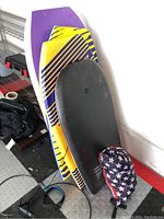 Five stacked boogie boards in various colors and sizes with an inflatable lounger bag beside them.