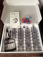 Full view of the set in the open box showing 32 cups, vacuum pump, valve attachments, and instruction booklet arranged neatly in molded packaging.