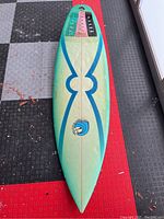 Top-down view of the surfboard showing blue design and logo, traction pads at tail, and nose shape.