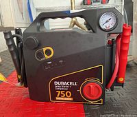 Front and side view of Duracell jump-starter and compressor unit showing branding, peak amps, power knob, and clamps.