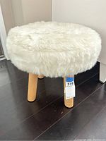 Photo showing round white faux fur cushioned top and three wooden legs of footstool.