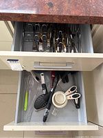 Bottom drawer containing kitchen utensils such as spatulas, whisk, measuring cups, kitchen scissors and peelers.