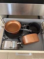 Drawer with Gotham copper and black pans and roasting pans stacked inside