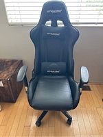 Front view of the black GTRACING gaming chair showing the seat, backrest, armrests, and neck/lumbar cushions.