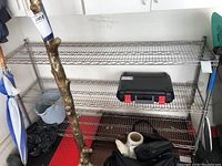 Front view of four-tier metal wire shelving unit with various items placed on shelves and around base.