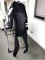 Full view of black Hurley wetsuit hanging on a metal rack, showing front side with gray chest panel and integrated feet booties.